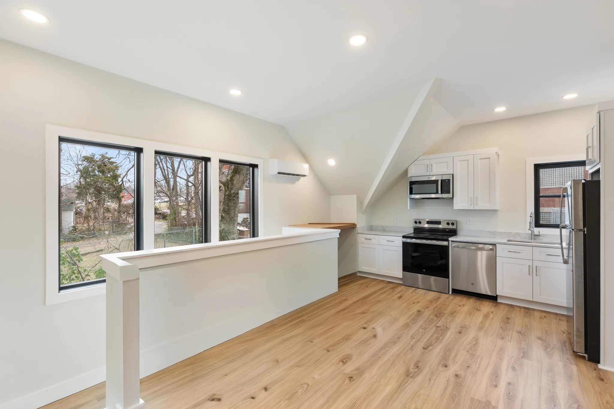 Upper-level kitchen with white shaker cabinets, stainless appliances, light wood-look flooring, a half-wall partition and black-framed windows