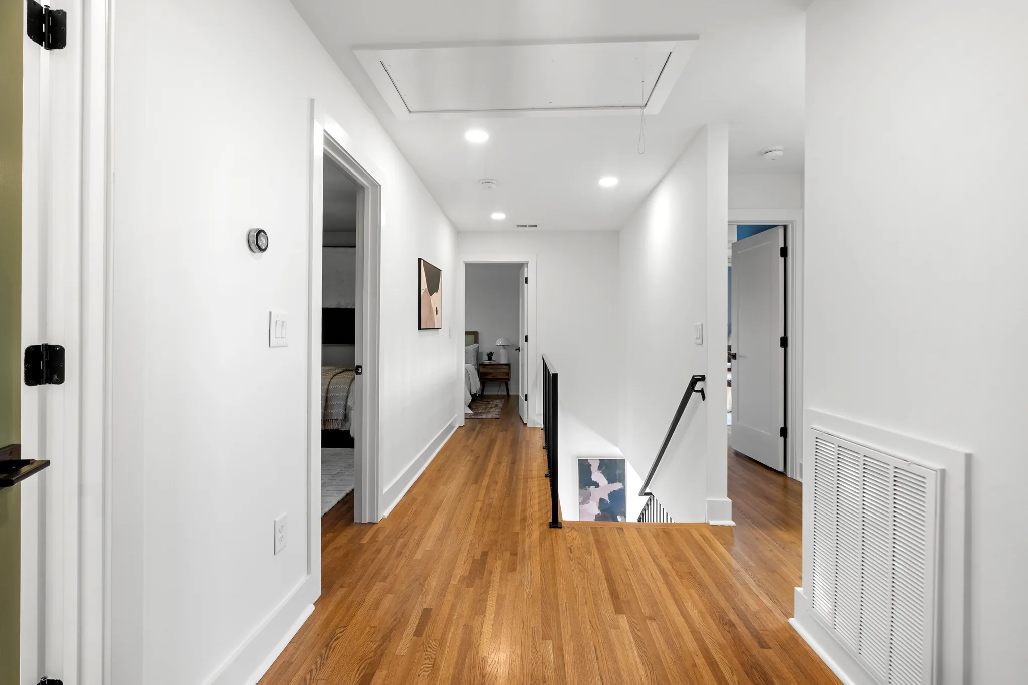 Upstairs hallway with red oak flooring, white walls and trim, black metal stair railing at the landing, and open doors to bedrooms