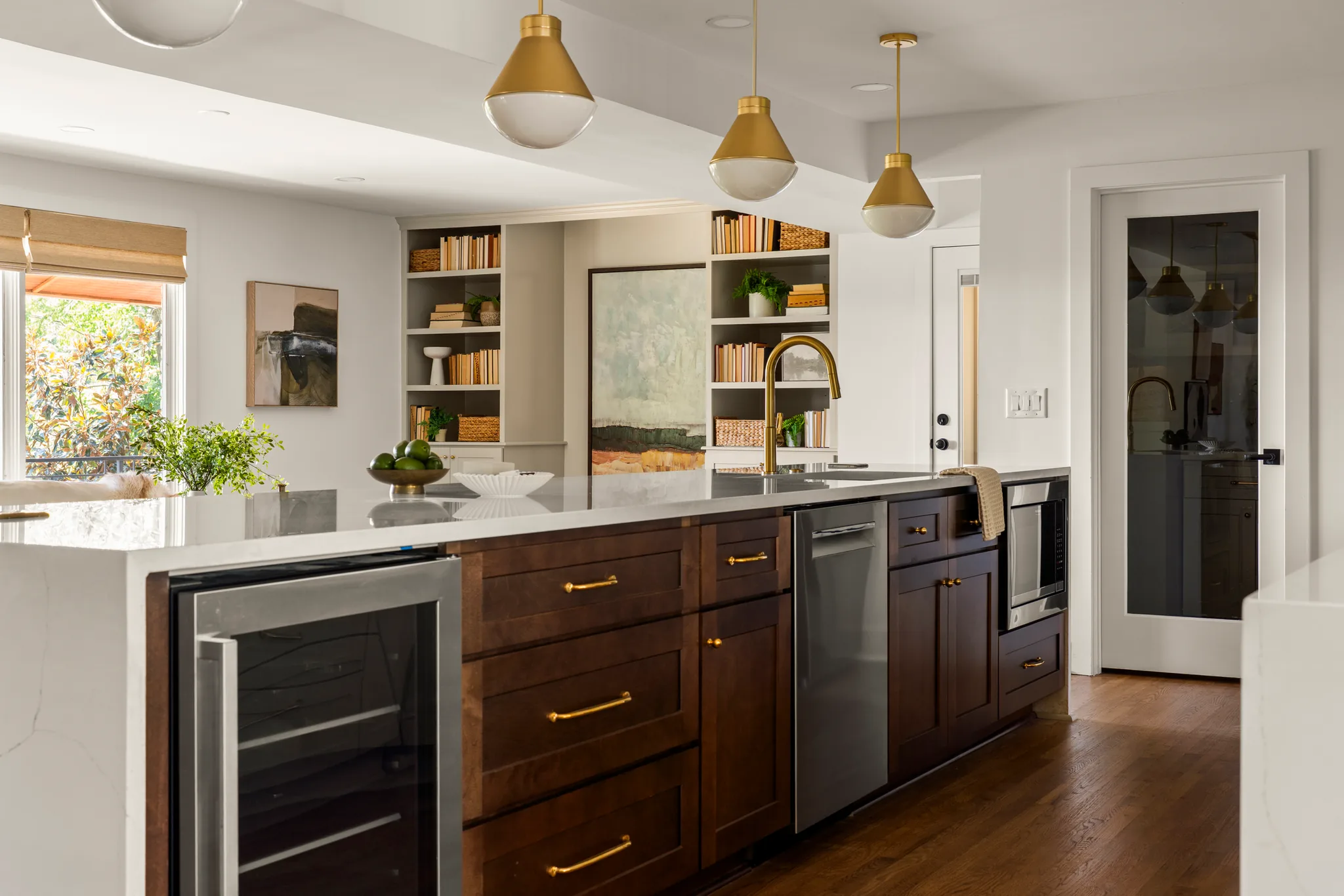 Kitchen island with dark walnut cabinets, white quartz waterfall counter, stainless beverage refrigerator and dishwasher, brass pendants overhead