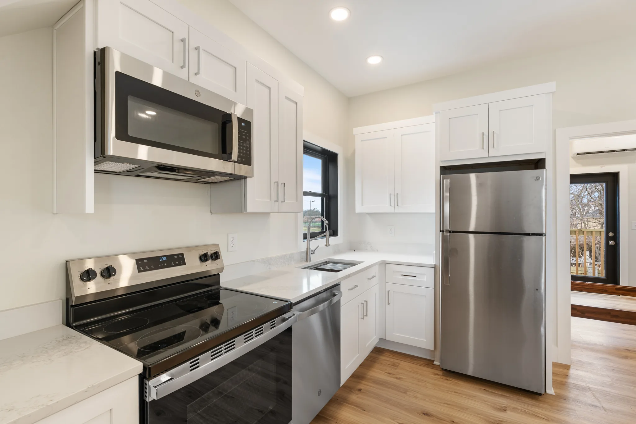 Kitchen with white shaker cabinets, speckled quartz counters, stainless range, microwave, dishwasher and top-freezer refrigerator on light wood floors