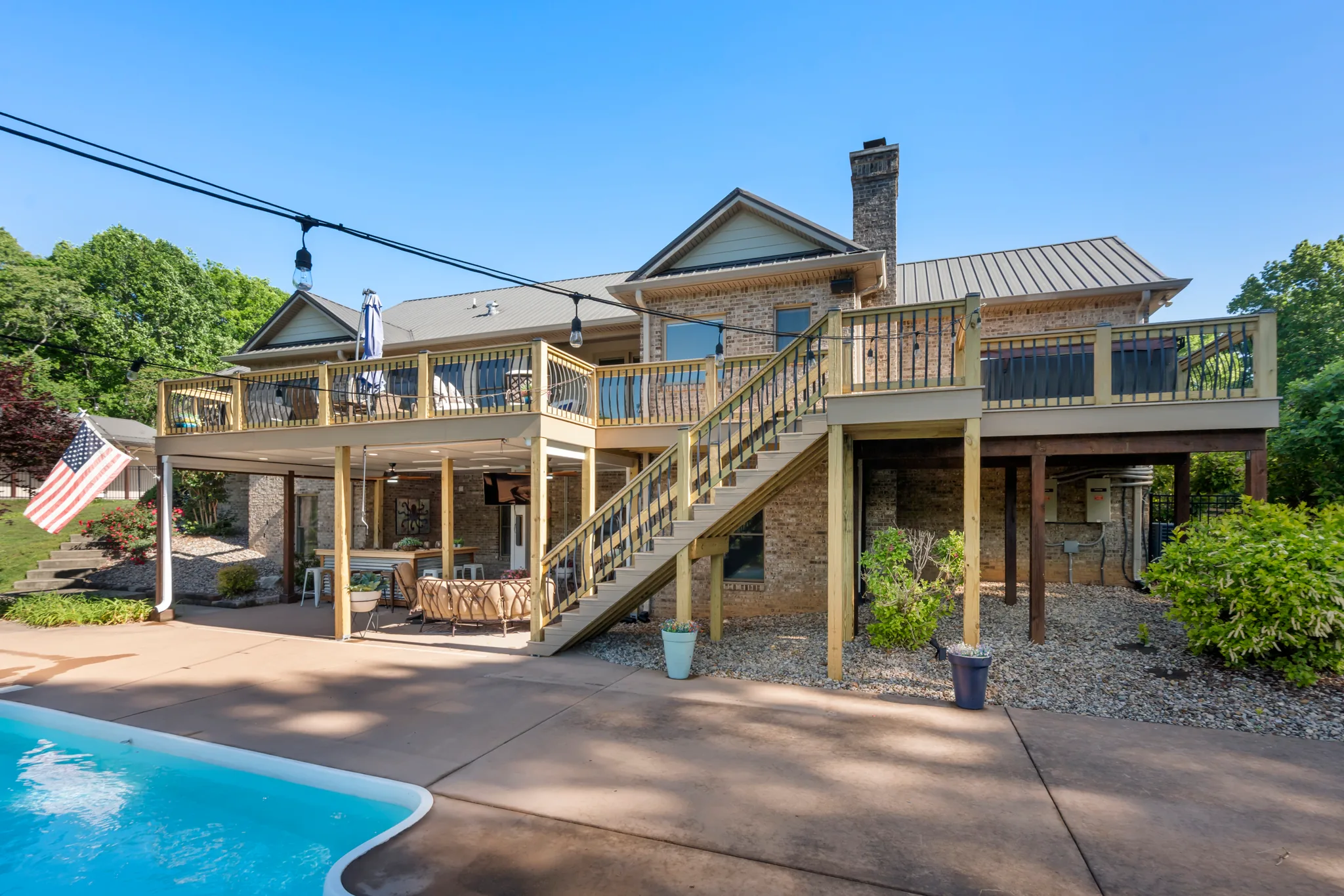 Elevated wood deck with black metal balusters and a long stair run on a brick home above a concrete pool patio